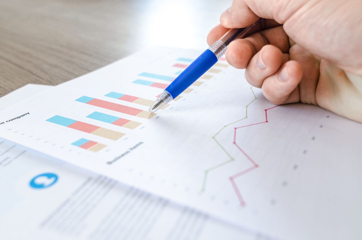 A hand using a pen to point at stacked bar and line charts on a printed business report