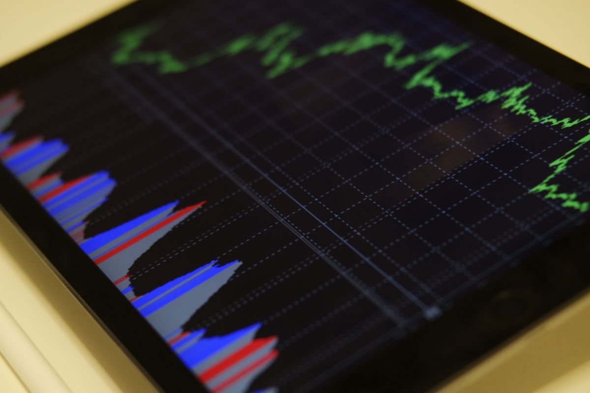 A tablet displaying a green price line chart and a volume indicator on a dark financial dashboard